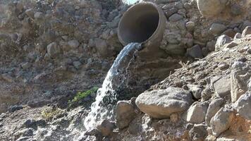 Waste water flows out of a sewage pipe into a sandy hole. video