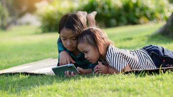 Two young girls lying on the lawn looking at their phones, summer, golden hour, sunset. SSTKHome photo