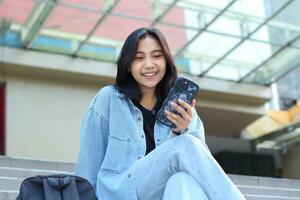 carefree smiling stylish asian young woman using smartphone app, video chat, online shop, and browsing social media while sitting in stairs of a mall outdoor wear casual photo