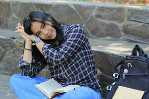 happy young asian woman college student with smiling face enjoy read a book for exam in the park photo