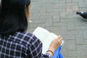 contento consciente de joven asiático mujer Universidad estudiante leyendo un libro en el parque, educación concepto foto