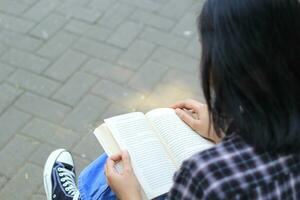 contento consciente de joven asiático mujer Universidad estudiante leyendo un libro en el parque, educación concepto foto