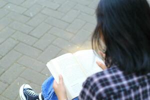 contento consciente de joven asiático mujer Universidad estudiante leyendo un libro en el parque, educación concepto foto