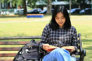 happy mindful young asian woman college student reading a book in the park, education concept photo