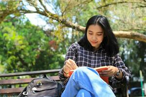 contento consciente de joven asiático mujer Universidad estudiante leyendo un libro en el parque, educación concepto foto
