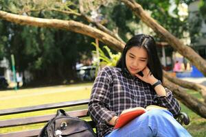 happy mindful young asian woman college student reading a book in the park, education concept photo