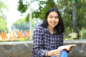 excited asian beautiful young woman college student smiling with happy face reading a book outdoor, campus university concept photo