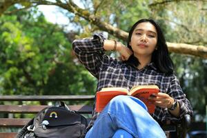 happy young asian woman college student with smiling face enjoy read a book for exam in the park photo