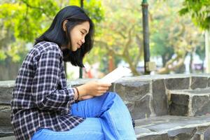 happy and succes female asian college student enjoying read a book in the park photo