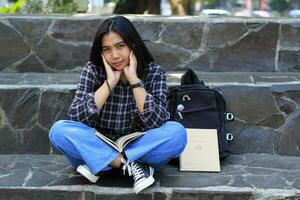 happy young asian woman college student with smiling face enjoy read a book for exam in the park photo