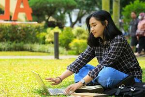 young smiling asian woman using laptop and writing notebook, cheerful asian student watching webinar and studying from e course photo