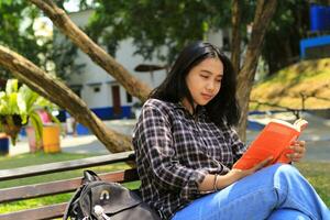 happy and succes female asian college student enjoying read a book in the park photo