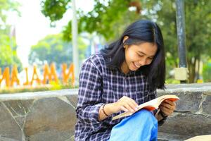 contento alegre asiático hembra estudiante leyendo un libro y riendo disfrutando vacaciones foto