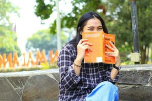 contento alegre asiático hembra estudiante leyendo un libro y riendo disfrutando vacaciones foto