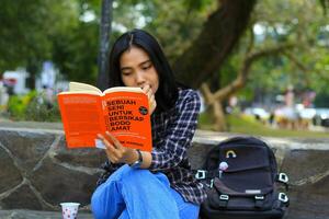 grave asiático mujer estudiante leer un libro pensar y hacer investigación para su deberes foto