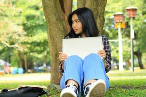 peaceful smiling asian beautiful woman remote worker using laptop browsing and communicating under tree, work from anywhere concept photo
