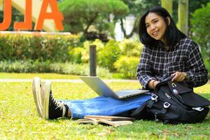 happy asian student using laptop and reading book to study for exam and surfing in the internet with excitement photo