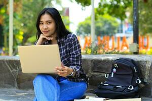young smiling asian woman using laptop and writing notebook, cheerful asian student watching webinar and studying from e course photo