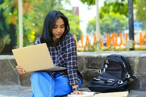 young smiling asian woman using laptop and writing notebook, cheerful asian student watching webinar and studying from e course photo