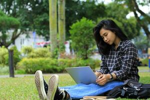 portrait of focused young asian woman surfing internet using laptop to working remotely, read book, and writing in notebook. attractive asian student study in outdoors photo