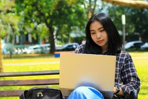 happy young asian woman focused using laptop  working remotely and browsing in social media in comfortable outdoors space photo