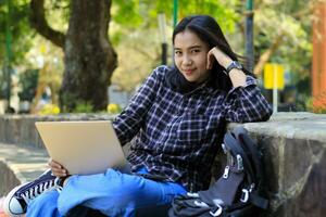 contento joven asiático mujer estudiante sonrisa trabajando en ordenador portátil hacer Lanza libre trabajo y deberes mirando a cámara foto