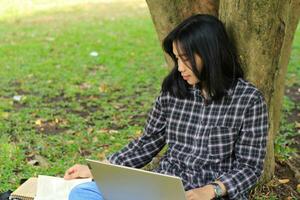 young smiling asian woman using laptop and writing notebook, cheerful asian student watching webinar and studying from e course photo