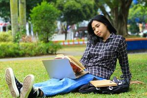 portrait of focused young asian woman surfing internet using laptop to working remotely, read book, and writing in notebook. attractive asian student study in outdoors photo