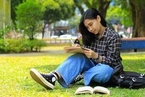 smiling asian beautiful young woman enjoy writing to do list and idea in notebook in outdoors city park photo