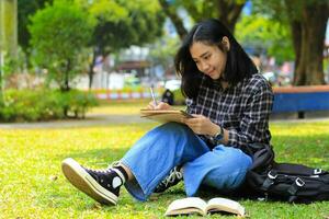 smiling asian beautiful young woman enjoy writing to do list and idea in notebook in outdoors city park photo