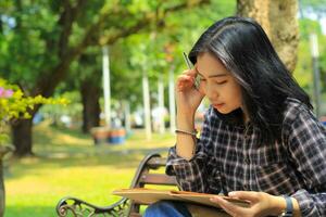 confusing asian young woman thinking an idea and writing in notebook with a pen in nature outdoors area photo