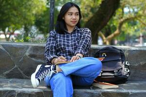 portrait of relax young asian woman writing idea and memories on notebook im outdoors area or park look away photo