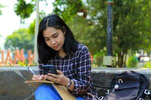 happy and joyful asian young bussines woman smiling hold mobile phone, writing in notebook or journal diary, student learning photo