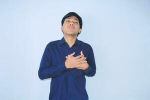 young asian man is relaxing from heart attack pain doing inhale and exhaling face expression and gesture wearing navy shirt photo