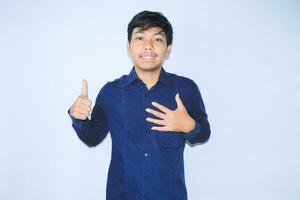 proud young asian man smiling with grateful face for survived from heart attack and has recovery is holding chest with thunbs up wearing navy shirt photo