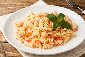 Spiral pasta mixed with cherry tomatoes and tomato sauce on a plate. photo