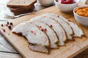 Pieces of smoked boiled pork on a wooden rustic Board with bread, sauces and spices on a wooden table photo