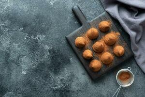 Delicious chocolate truffles sprinkled with cocoa powder and walnuts on a wooden stand. Dark concrete background. Copy space. photo