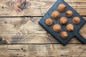 Delicious chocolate truffles sprinkled with cocoa powder on a wooden stand. Wooden background. Copy space. photo