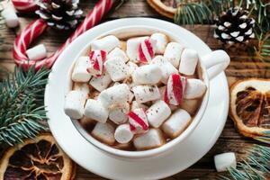 A Cup of hot chocolate with marshmallows. Christmas tree and decorations, cane caramel and oranges nuts Wooden background photo