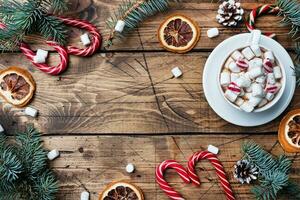 A Cup of hot chocolate with marshmallows. Christmas tree and decorations, cane caramel and oranges nuts Wooden background copy space. photo