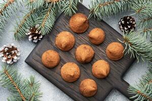 Delicious chocolate truffles sprinkled with cocoa powder on a wooden stand. Christmas tree scenery concept. photo