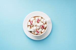 Cup of hot chocolate with marshmallow cocoa powder and caramel on pastel blue background with copy space. Christmas winter concept. photo