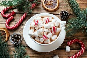 A Cup of hot chocolate with marshmallows. Christmas tree and decorations, cane caramel and oranges nuts Wooden background photo