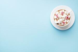 Cup of hot chocolate with marshmallow cocoa powder and caramel on pastel blue background with copy space. Christmas winter concept. photo