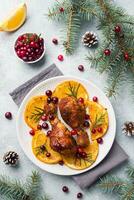 Baked chicken drumstick with oranges and cranberries in a plate light grey background. Christmas food Table with decorations. photo