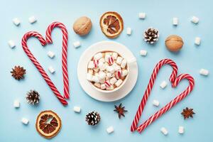 Cup of hot chocolate with marshmallow cocoa powder and caramel nuts, oranges on pastel blue background with copy space. Christmas winter concept. photo