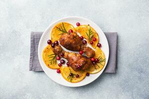 Baked chicken drumstick with oranges and cranberries in a plate light grey background. Christmas food Table with decorations. Copy space. photo