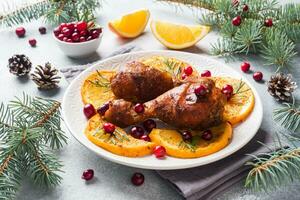 Baked chicken drumstick with oranges and cranberries in a plate light grey background. Christmas food Table with decorations. photo