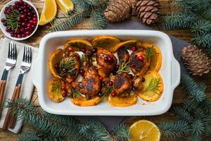 Baked chicken drumstick with oranges and cranberries in a baking sheet on a wooden background. Christmas food Table with decorations. photo